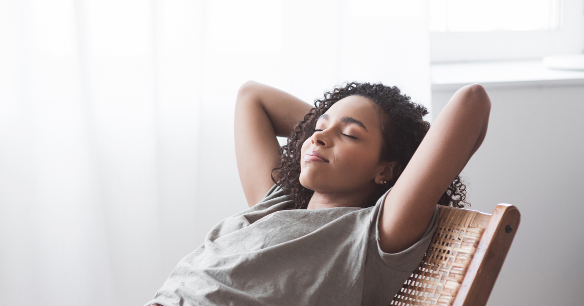 Image of a woman doing nothing. Relaxing with eyes closed, leaning back and arms up and bent with hands behind her head