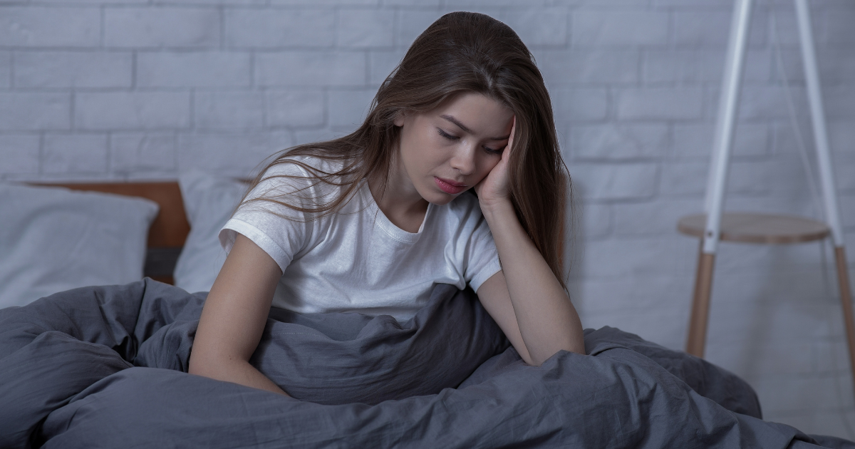 SAD Seasonal Affective Disorder woman in bed sitting up looking down resting her head on her hand