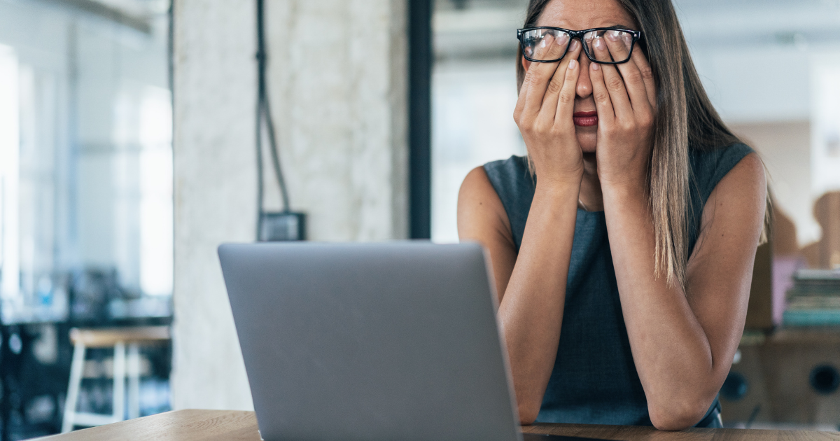 Impostor Syndrome woman at desk with head in hands in front of laptop