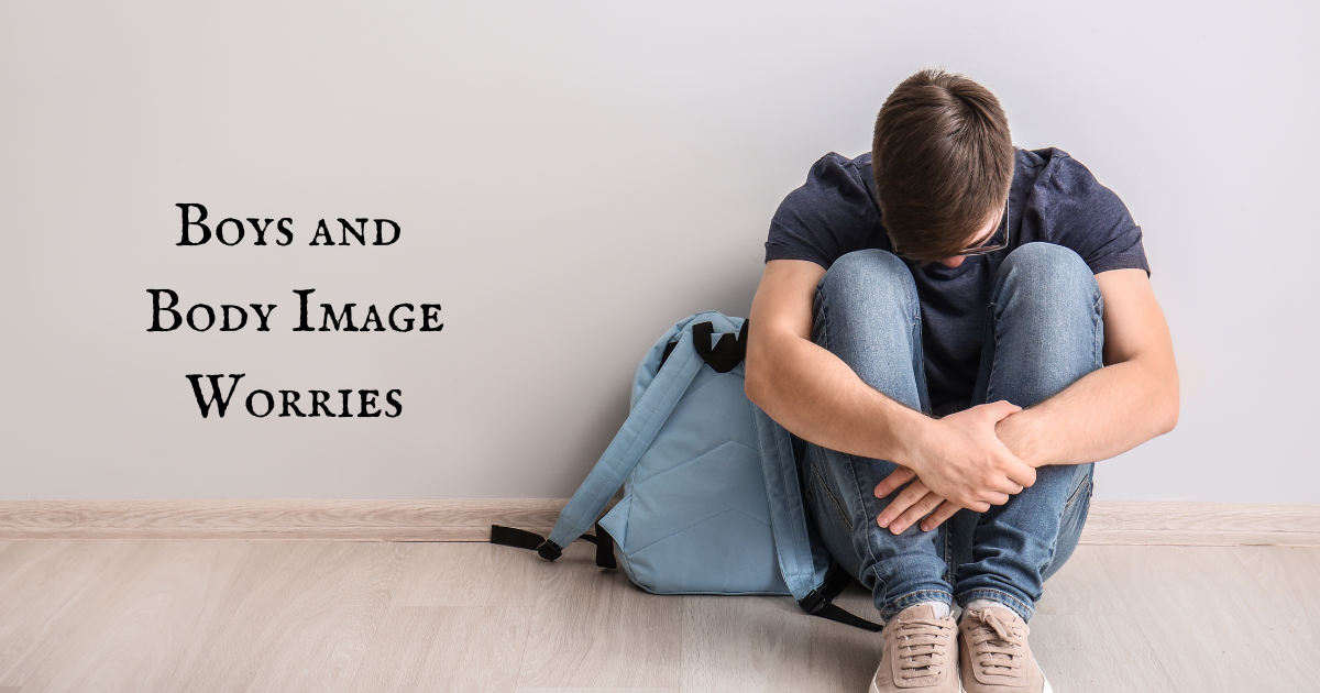 Boys and Body Image. Teenage boy sat on the floor with his head down and hands folded over his legs.